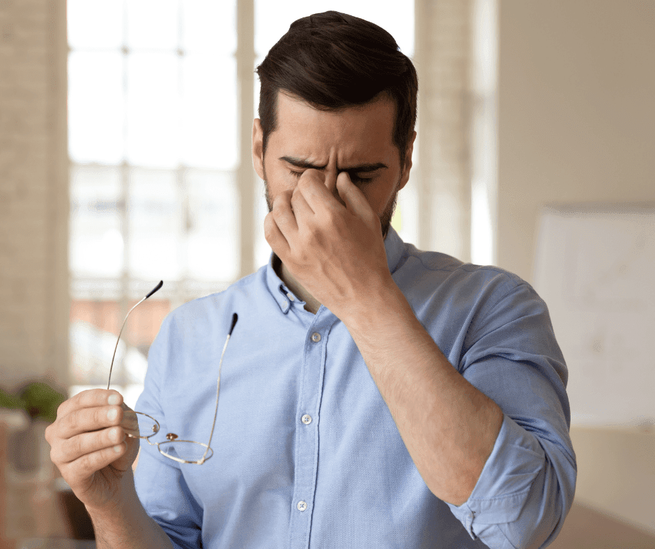 Man met blauw overhemd heeft last van vermoeide ogen